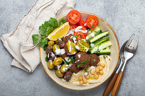 Falafel salad bowl with hummus, vegetables, olives and herbs. Vegan lunch plate top view, rustic stone background, healthy meal with falafel and veggies