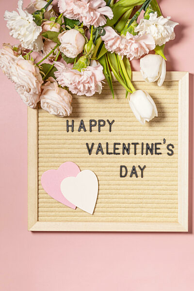 Happy Valentine's Day lettering on letter board and beautiful spring flowers on light pink background. Valentine's day, Womans day, mothers day greeting card. View from above. Copy space.