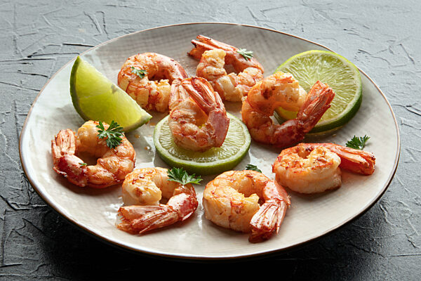 Shrimps. Cooked shrimp with lime on a white plate, on a black stone table