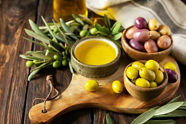 Freshly picked olives berries in wooden bowls and pressed oil served on old wooden boards. Copy space.