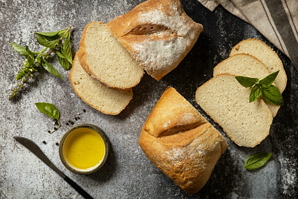 Sliced Italian ciabatta bread with extra virgin olive oil and herb on a dark stone background. Fresh crispy Ciabatta bread. View from above.
