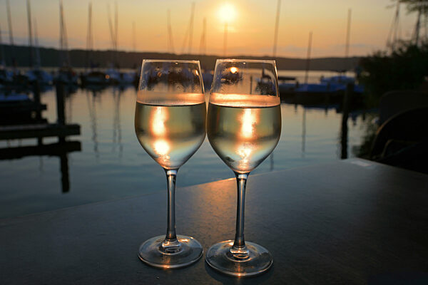 Two glasses of cold white wine at sunset at the marina with sailboats on the calm water, beautiful summer evening on vacation, copy space, selected focus