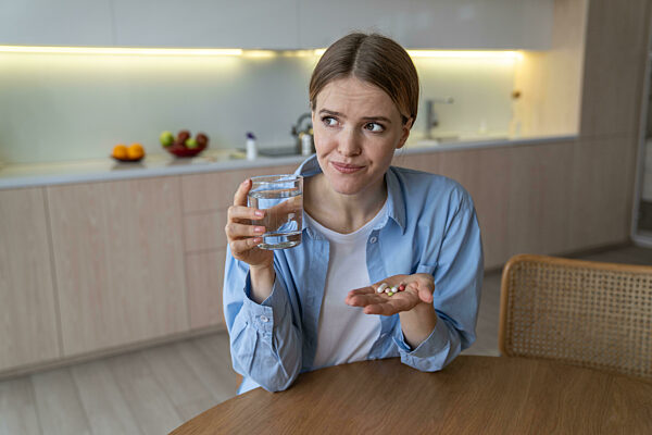Eine unglückliche Frau schneidet Grimassen, ist sich ihrer Verschreibung nicht sicher und nimmt Tabletten gegen schwere Depressionen. Kranke Tage