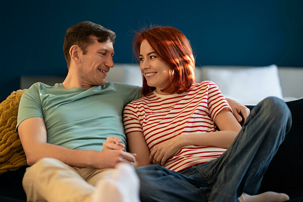 Verliebtes Ehepaar, das sich zärtlich anschaut und die Hände hält, teilt aufrichtige Gefühle auf der heimischen Couch