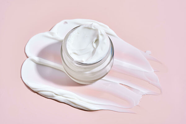 An open jar of cream with its texture on a pink background.