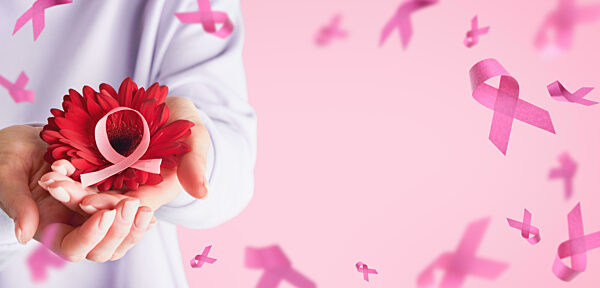 Rosa Brustkrebs-Bewusstseins-Schleife. Weibliche Hände halten rote Gerbera mit fliegenden rosa Schleife auf rosa Hintergründen. Brustkrebs Bewusstsein und Oktober Rosa Tag, Weltkrebstag. Ansicht von oben. Mock up.