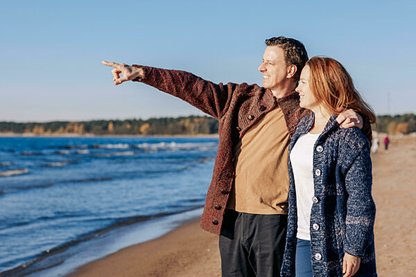 Verliebtes Paar geht am Strand am Meer entlang an einem sonnigen Herbsttag. Wochenende und Lifestyle-Konzept