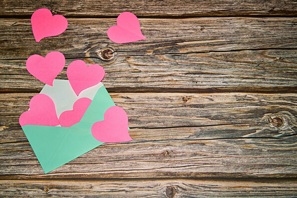 A light green envelope brimming with pink hearts in a rustic wooden envelope