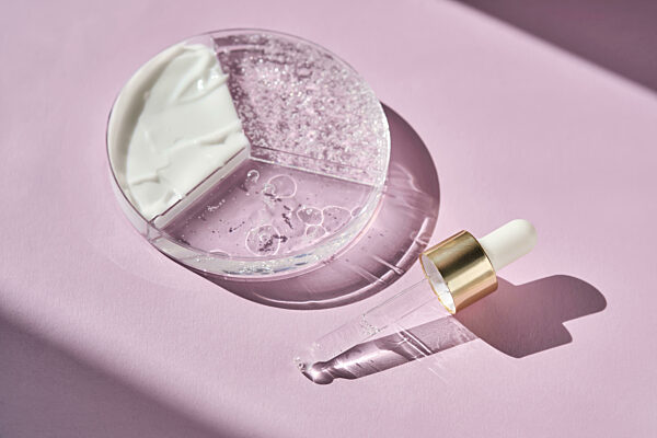 Eine dreiteilige Petrischale mit kosmetischen Pflegeprodukten und einer Pipette auf violettem Hintergrund.