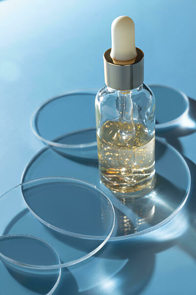 Forschung im Hautpflege-Labor. Kosmetikproduktion, Extraktion von Komponenten aus 24k-Goldflocken. Hautpflege Kosmetologie Tests. Petrischale mit Tropfflasche auf blauem Hintergrund
