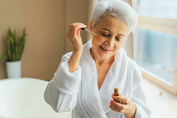Woman applying natural drops cosmetics oil to face skin...