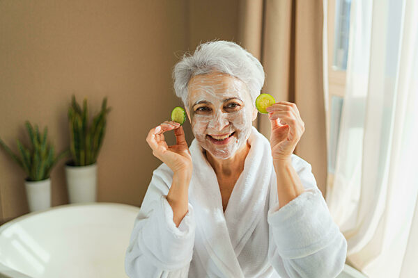 Mature adult old woman with nourishing anti age face cream mask holding...