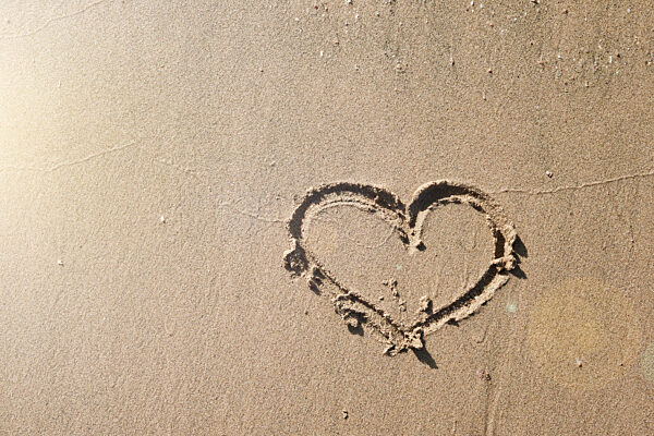 Herz in Sand auf leeren tropischen Strand bei Sonnenuntergang gezeichnet. Urlaub und Reisen Konzept. Valentinstag oder Hochzeit Konzept.