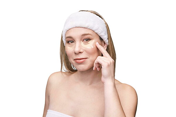 Kaukasische weibliche erwachsene Anwendung unter Augenmaske für Hautpflege Routine mit Kopfband und nackten Schultern.