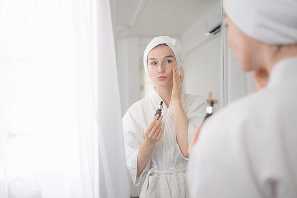 Eine junge Frau steht vor einem Spiegel und pflegt ihr Gesicht