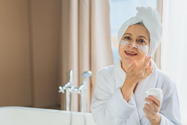 Reife erwachsene alte Frau, die nährende Anti-Age-Gesichtscreme aufträgt und ihre tägliche Schönheitsroutine durchführt Ältere Frau mit weißer Maske oder Creme auf der Haut erhält Gesichtsbehandlung Hautpflege Alterung Schönheit Hautpflege Kosmeti