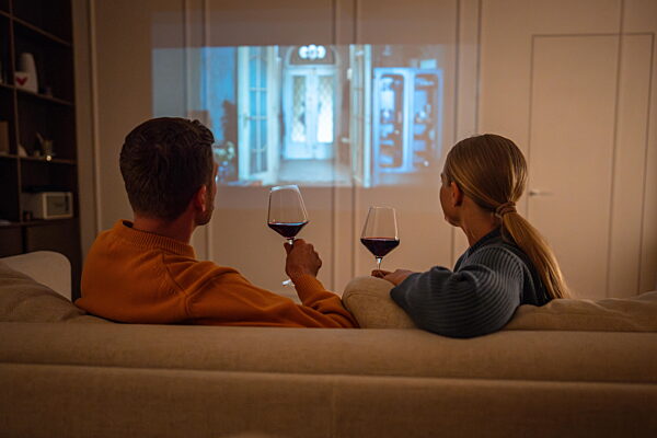 Paar genießt romantischen Abend mit Wein und Film auf dem Bildschirm zu Hause auf dem Sofa Rückansicht projiziert