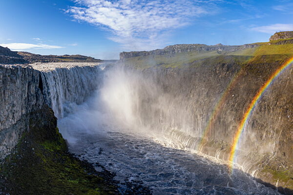 Blick auf den majestätischen Wasserfall Dettifoss im Nordosten Islands mit einem doppelten Regenbogen an einem schönen Sommertag
