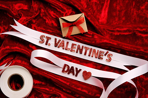 Festlicher Hintergrund mit dem Schriftzug St. Valentine's Day mit rotem Samt und weißer Schleife.