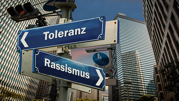 Ein Bild mit einem Schild, der in zwei verschiedene Richtungen auf Deutsch zeigt. Eine Richtung weist auf Rassismus, die anderen Punkte auf Toleranz. - Bildmontage