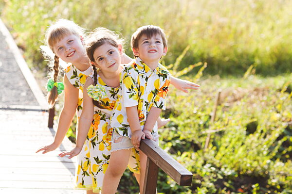 Drei fröhliche Kinder spielen vor der Kamera im Sommer auf dem Kopf stehend und lächeln in die Kamera.