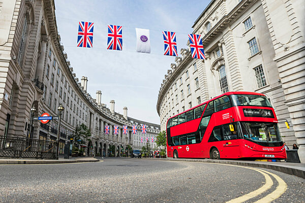 A traditional red double decker London bus at Piccadilly Circus under rows of Union Jack flags.