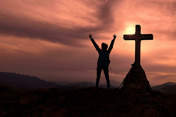 Cross At The Top Of The Mountain With A Mountaineer Who Raises His Hands