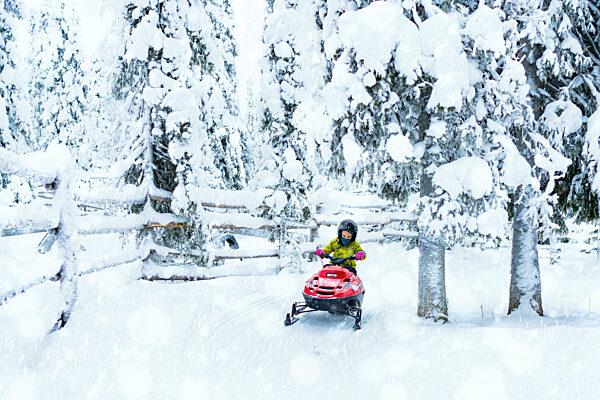 Happy young boy driving a snowmobile in the Arctic forest, Lapland, Finland