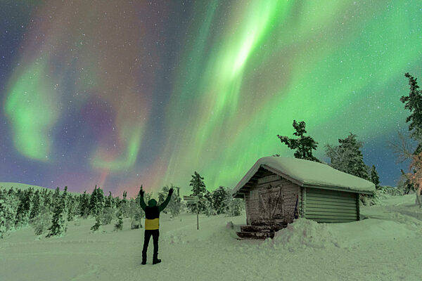 Happy tourist waving at the northern lights (aurora borealis) dancing in the night sky above the arctic circle, Akaslompolo, Kolari municipality, Finland, Scandinavia, Europe