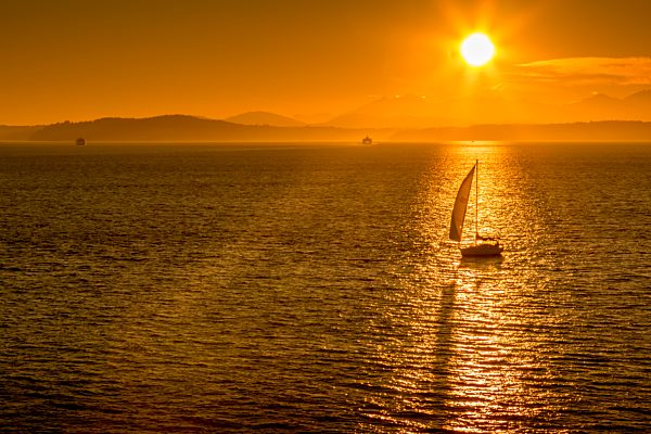 Sailing boat and sunset over Elliott Bay with Bainbridge Island visible on the horizon viewed from Bell Harbour Marina. Seattle, Washington, USA, North America