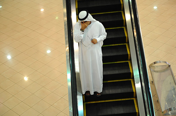 In arabischer Kleidung fährt ein Mann auf einer Rolltreppe in einem...