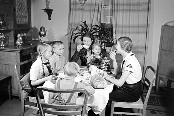 Eine Mutter sitzt mit fünf Kinder beim Frühstück am Küchentisch; Deutschland 1930er Jahre. A mother and her five chidren having breakfast at the kitchen; Germany 1930s.