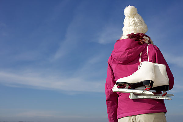 Frau in Winterkleidung mit Schlittschuhen unter blauem Himmel - Wetter - Jahreszeit - Wintersport