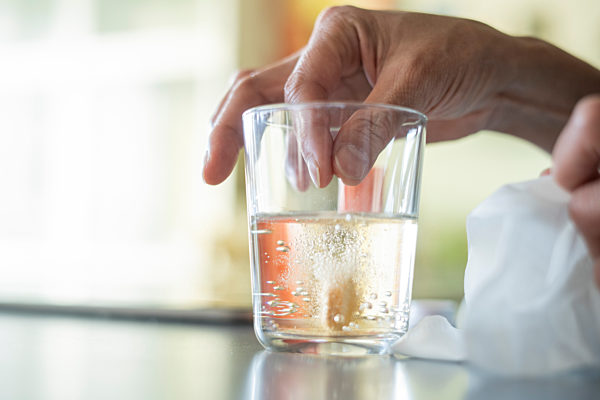 Close-up of woman's hand dropping pill in glass of water