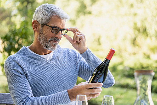 Mature man looking at wine bottle while sitting on chair