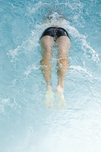 Man swimming in pool, low section, rear view