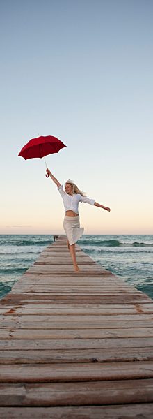 Young woman jumping on pier holding umbrella