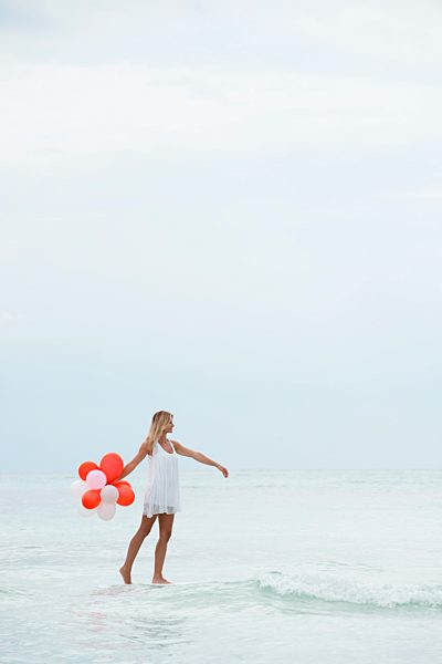 Woman walking on water, carrying bunch of balloons