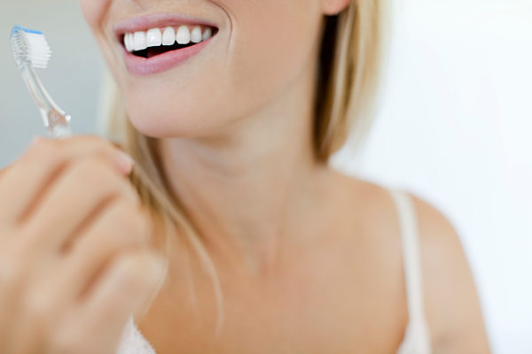 Smiling woman brushing teeth, cropped