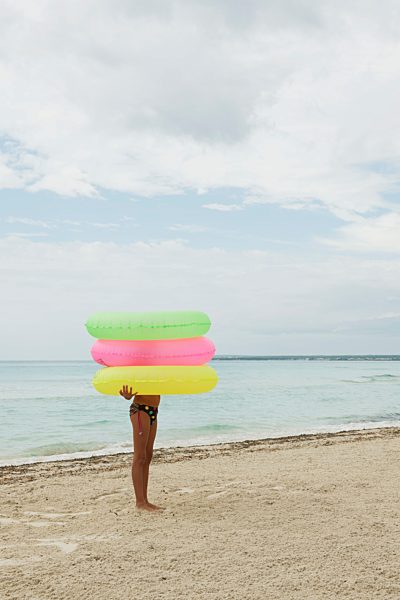 Girl holding stack of inflatable rings on beach, face obscured