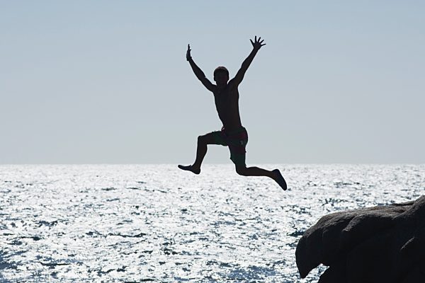 Teenage boy jumping into ocean, silhouette