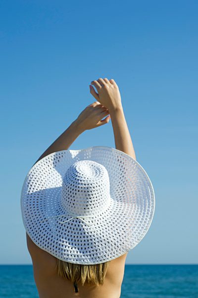 Woman wearing sun hat at the beach, rear view
