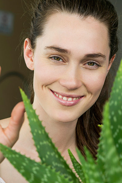 Young woman looking through aloe vera plant and smiling cheerfully