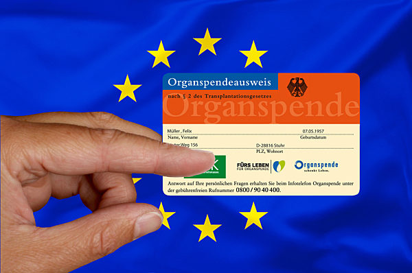 Hand mit Organspendeausweis vor EU-Fahne,