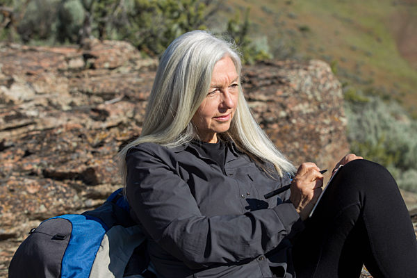Older Caucasian woman leaning on rock writing in journal, aeltere kaukasische Frau auf Felsen im Journal lehnt schriftlich