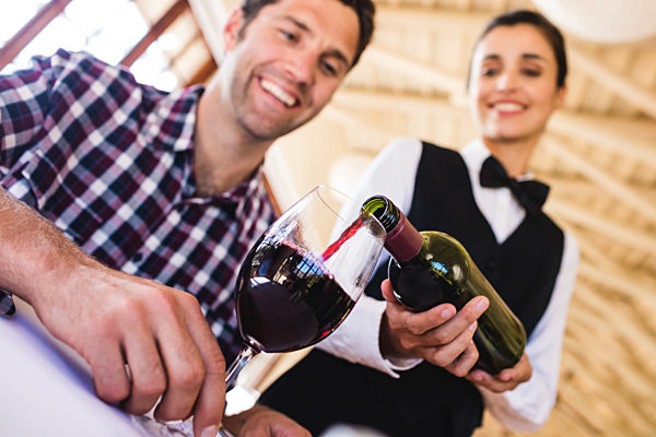 Waitress pouring red wine in wine glass at table