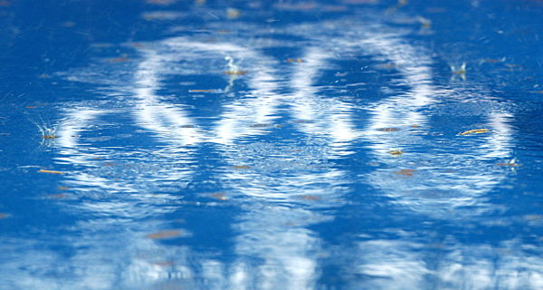 Raindrops fall into a puddle where the Olympic Rings are reflected at the...