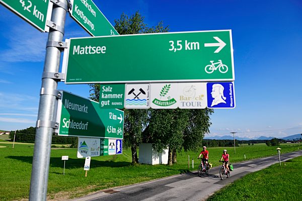 Paar mit E-Bikes vor Radwege-Schildern, Schleedorf, Salzburger Seenland, Salzburger Land, Österreich, Europa