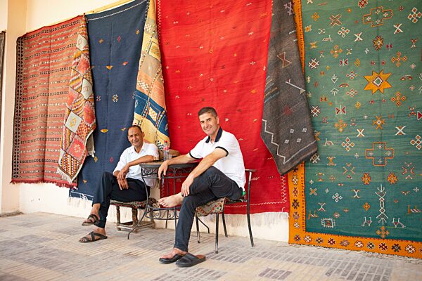 Marokkanische Männer machen eine Kaffeepause, hinten hängen handgeknüpfte Teppiche an der Wand, Meknès, Marokko, Afrika