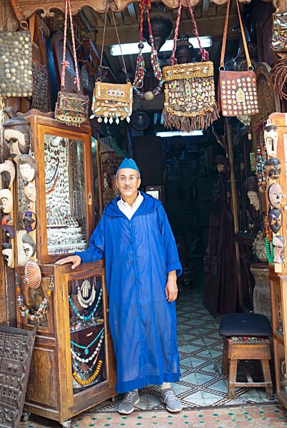 Marokkanischer Mann im traditionellen Djelabba oder Kapuzenmantel am Eingang zu seinem Shop, Fes, Marokko, Afrika